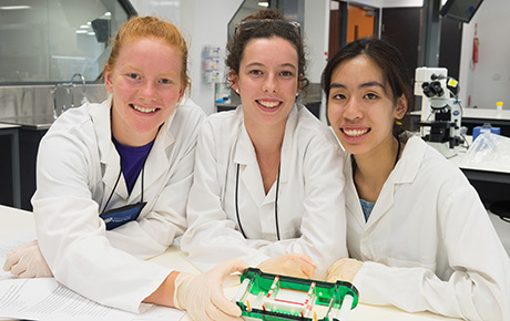 Three students in lab looking at equipment