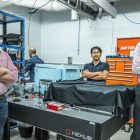 Co-founders of Quantum Brilliance (from left): CSO and NYSF alum Dr Marcus Doherty, COO Mark Luo, and CEO Dr Andrew Horsley. The three men are standing in a tech lab around a table covered in wires and tools.