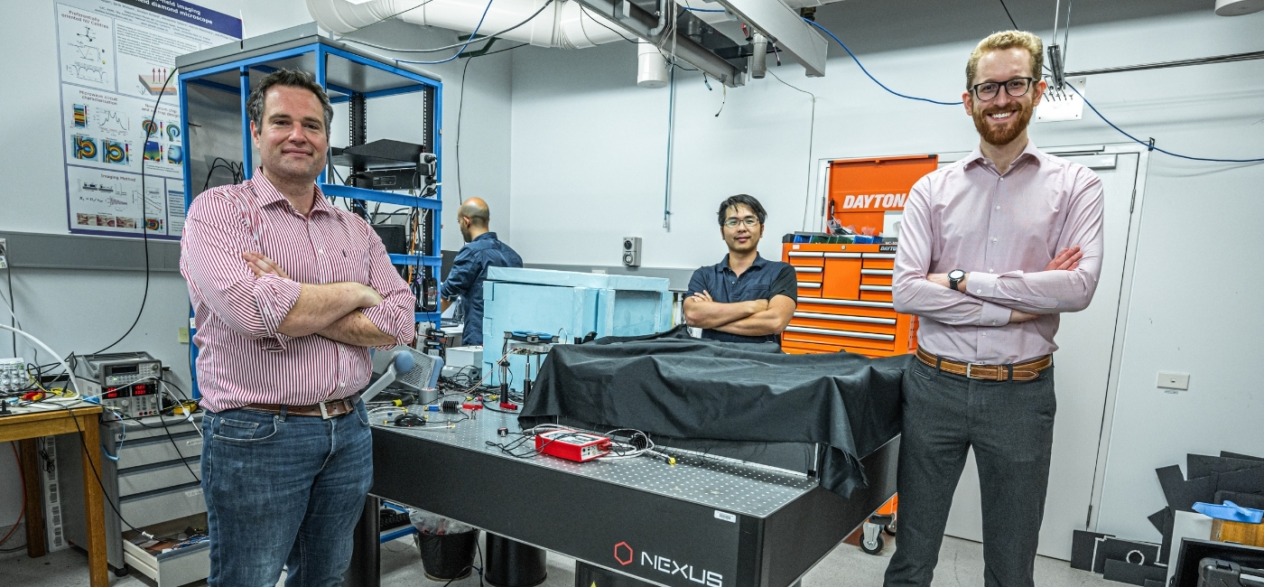 Co-founders of Quantum Brilliance (from left): CSO and NYSF alum Dr Marcus Doherty, COO Mark Luo, and CEO Dr Andrew Horsley. The three men are standing in a tech lab around a table covered in wires and tools.