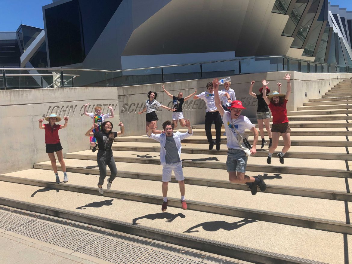 2021 NYSF Year 12 Participants are jumping into the air on the stairs in front of the John Curtin School of Medical Research