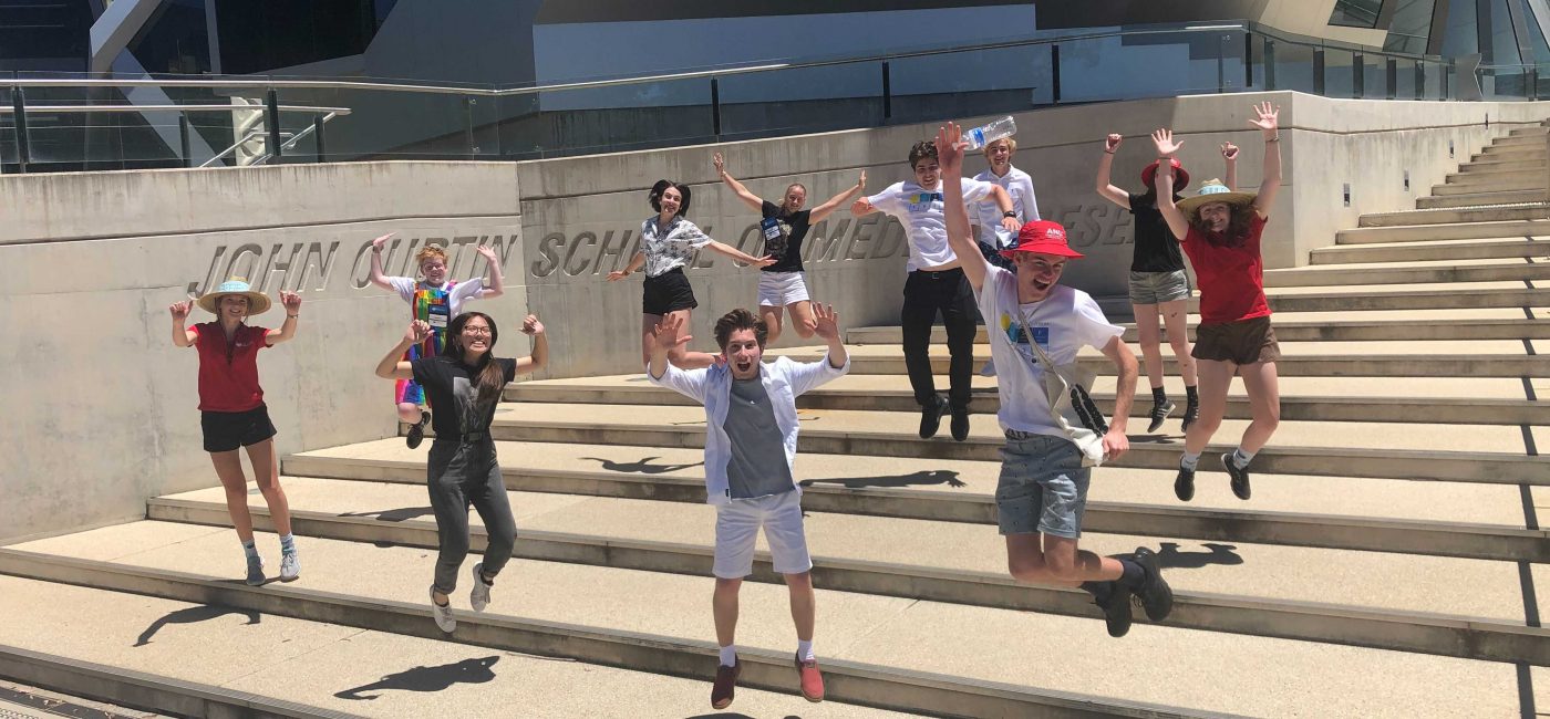 2021 NYSF Year 12 Participants are jumping into the air on the stairs in front of the John Curtin School of Medical Research